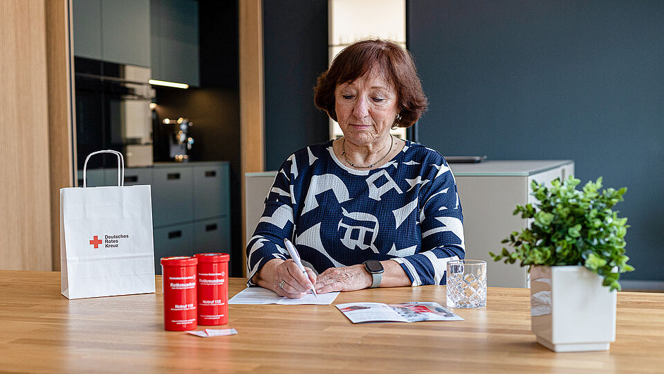Das Bild zeigt eine ältere Dame beim ausfüllen des Formulares mit ihren persönlichen Daten. Dieses wird anschließend in die Rotkreuzdose eingelegt.
